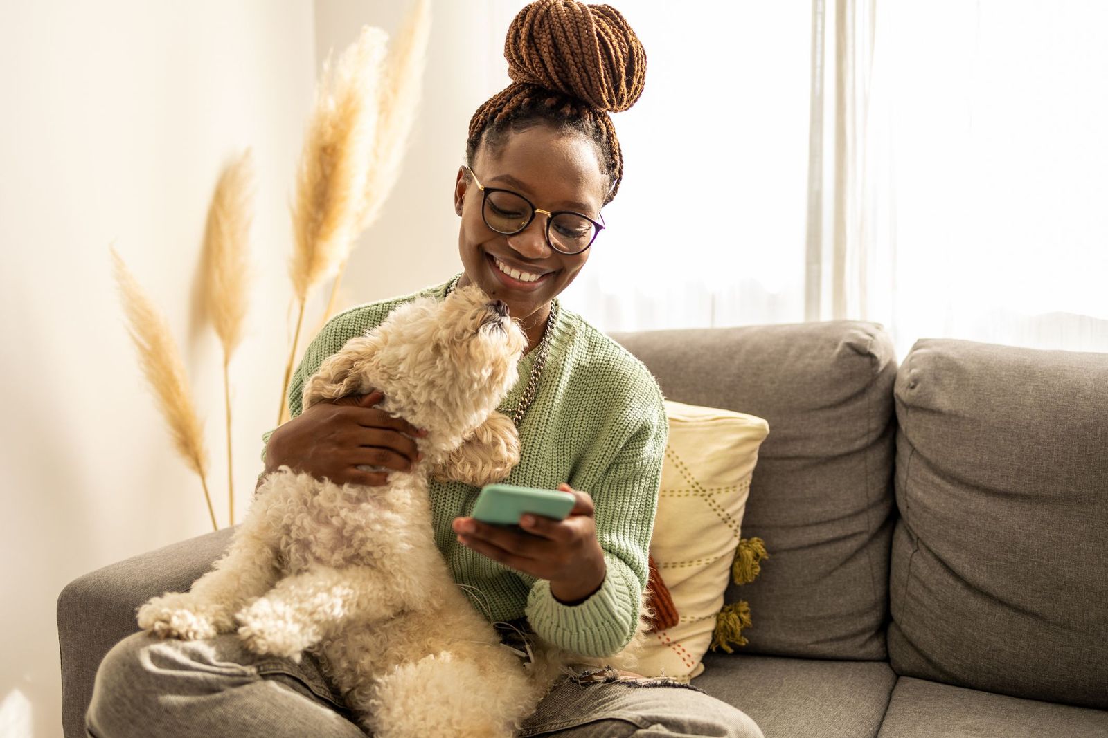 Providing a great virtual care experience - Small poodle mix dog licks owners face while sitting on the couch. Owner looks at her phone.
