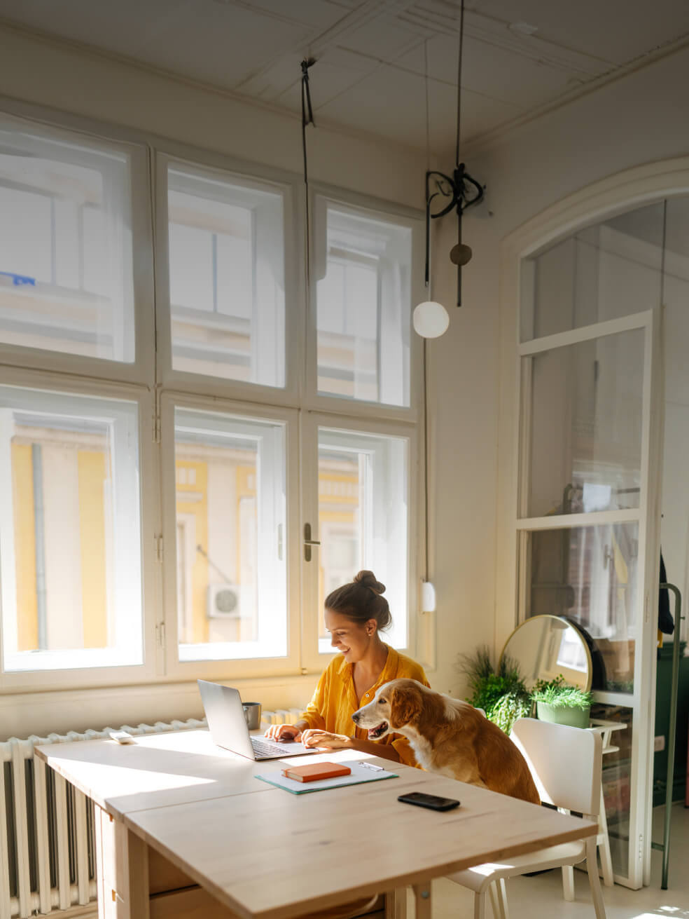 A woman working at a desk in a home office with her dog by her side