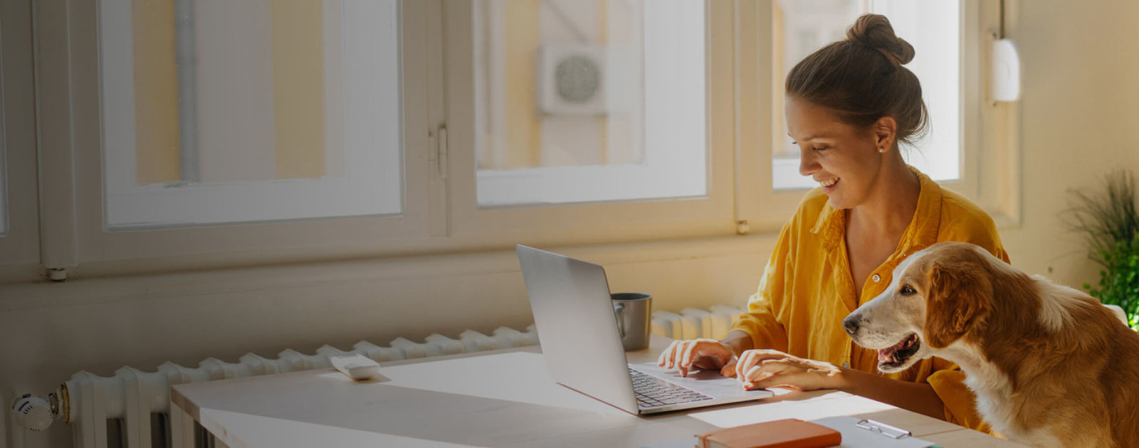 A woman working at a desk in a home office with her dog by her side