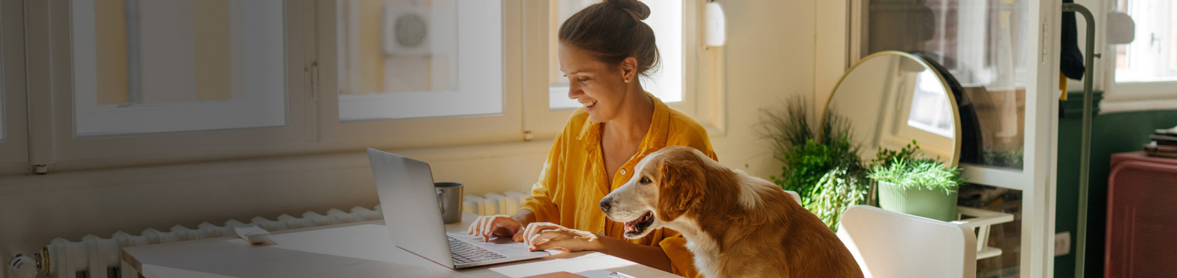 A woman working at a desk in a home office with her dog by her side