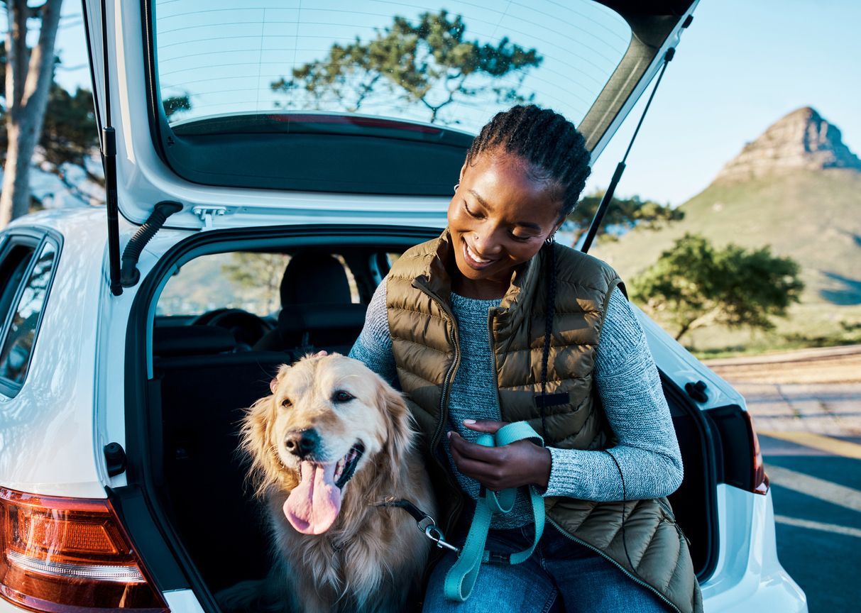 Road trip tips for traveling with your pup - A woman and dog sitting in the back of a parked hatchback