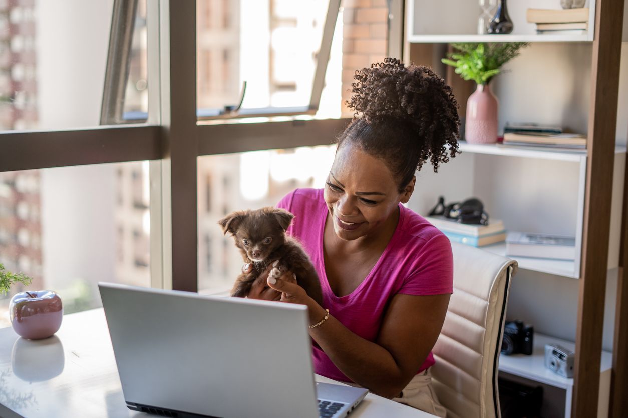 How much does an online vet cost? - A woman sitting at a table, holding her puppy up to her laptop 